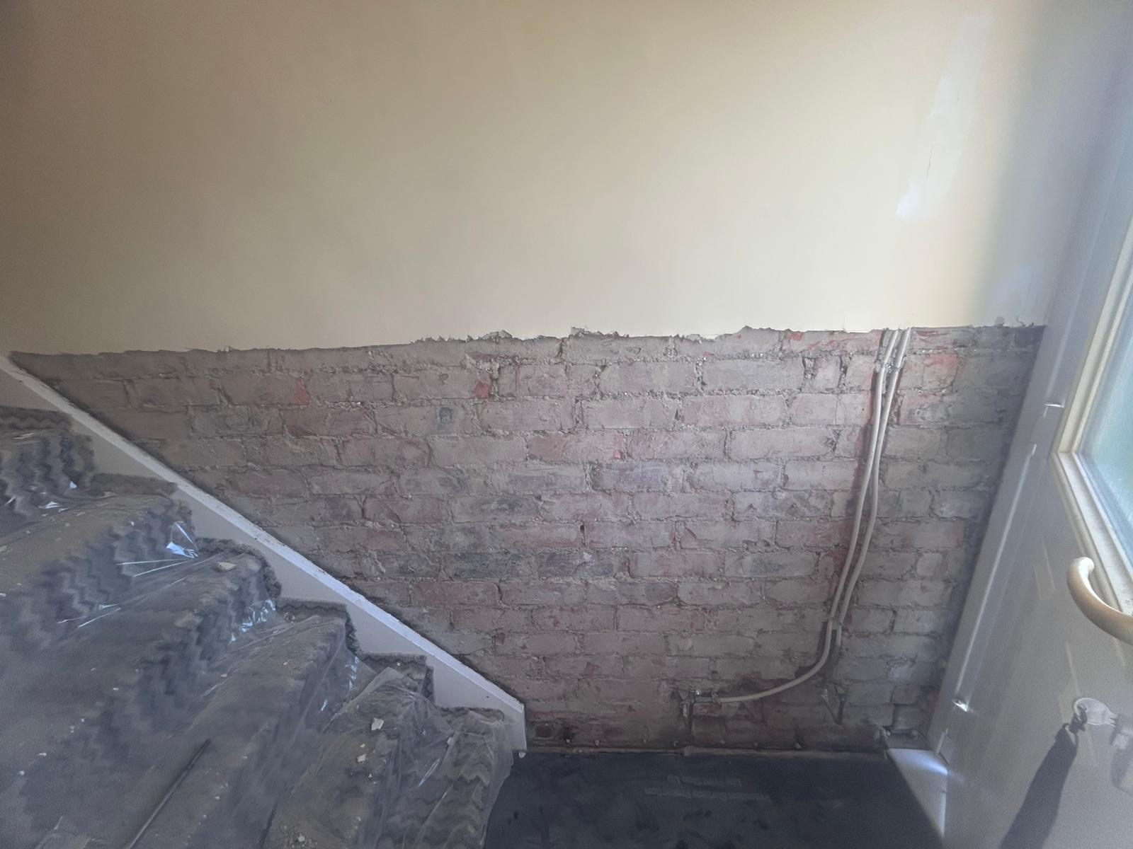 A lower wall hacked back to brick alongside a staircase during damp proofing