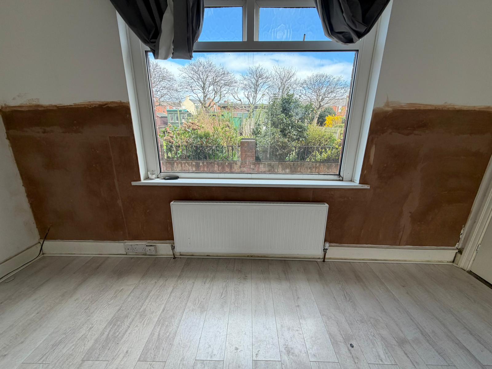 A replastered wall around a window with dust sheets protecting the floor