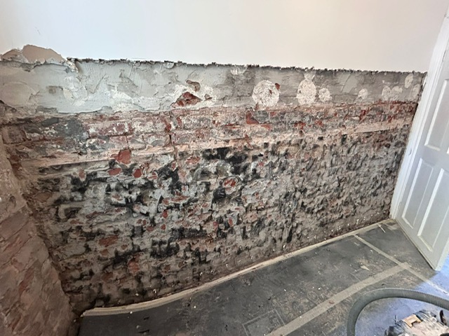 A wall hacked back to masonry showing the salt damaged plaster removed