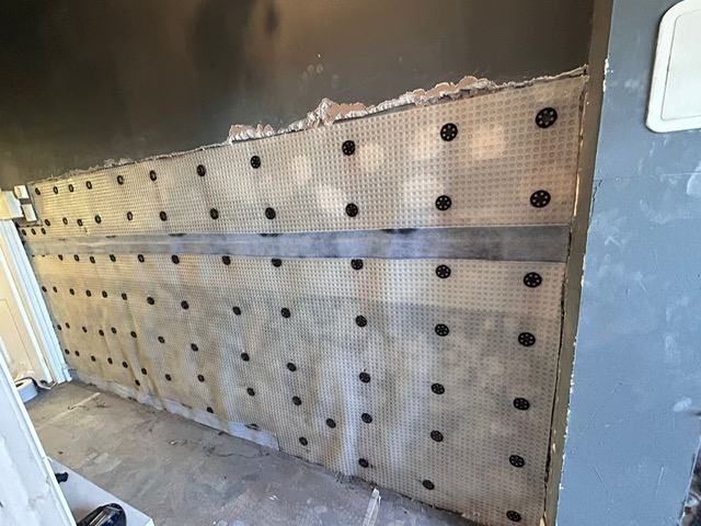 Tanking membrane installed across a wall at skirting level with fixing plugs