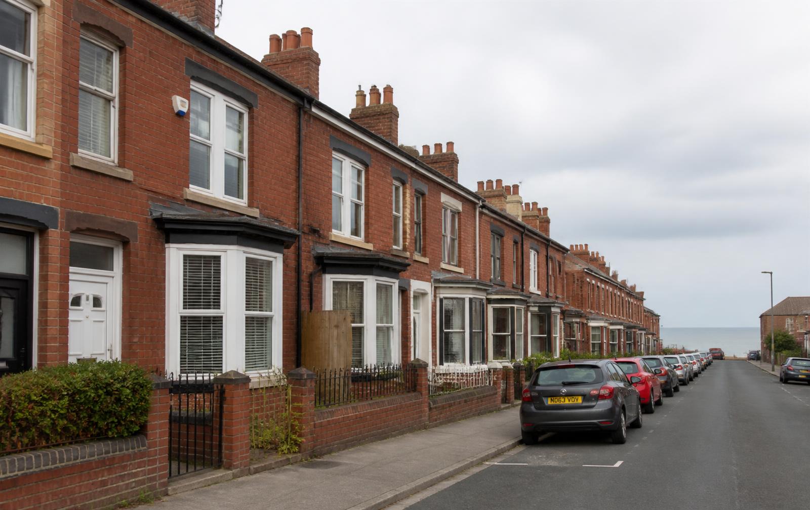 A row of red brick terraced houses with bay windows leading down towards the sea