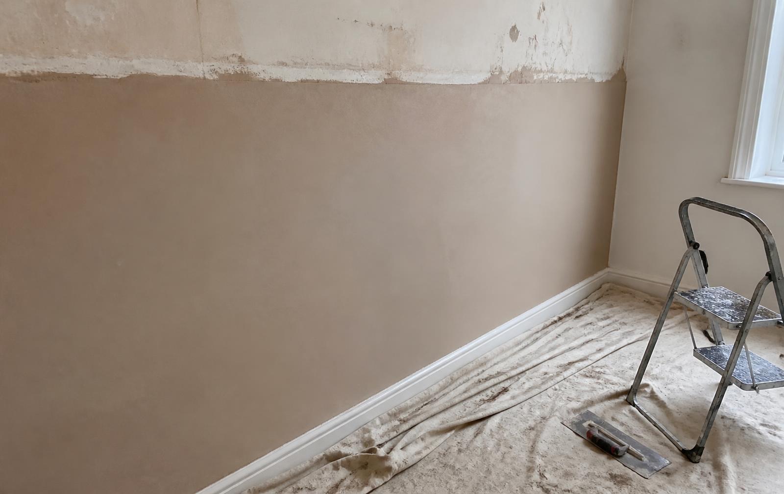 A freshly replastered lower wall with dust sheets and a plastering trowel on the floor